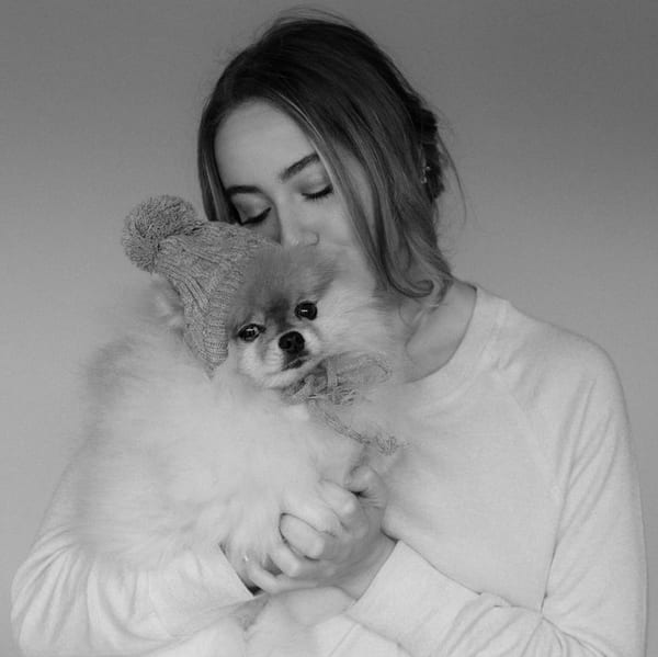 A woman holding and kissing a fluffy Pomeranian wearing a knit bobble hat